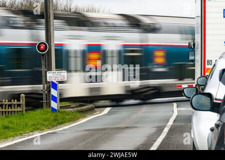 Passage à niveau ferroviaire sur une route de campagne avec porte ferroviaire automatique. Portails automatiques abaissés, portails fermés, feu clignotant rouge et voitures à l'arrêt Banque D'Images