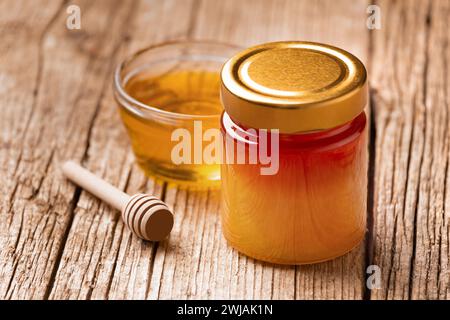 Miel bio dans un bocal en verre fermé et dans un bol en verre transparent, godet en bois sur un fond en bois rustique, gros plan. Banque D'Images