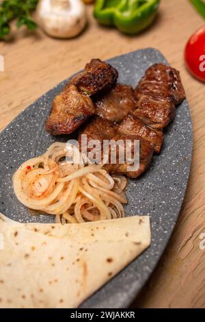 Viande et légumes grillés sur une table en bois rustique avec du pain plat mou. Viande succulente, légumes tendres, tomates vibrantes, poivrons, champignons, oignons Banque D'Images