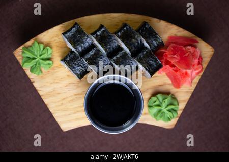 Assortiment de sushis avec une variété de rouleaux et de sashimis magnifiquement disposés sur une assiette en bois, accompagnés de baguettes et d'un côté de soja salé Banque D'Images