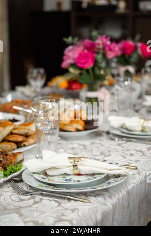 Table élégante avec roses roses, assiettes, argenterie, verres en cristal sur une nappe à motifs Banque D'Images