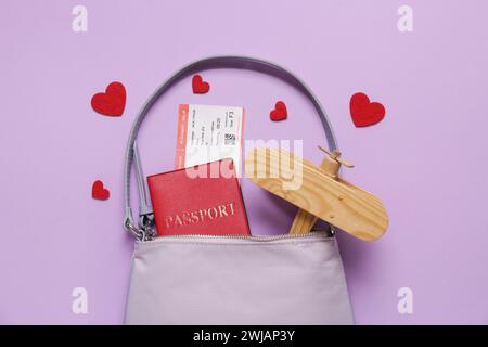 Sac avec passeport, avion en bois et coeurs sur fond lilas. Célébration de la Saint-Valentin Banque D'Images