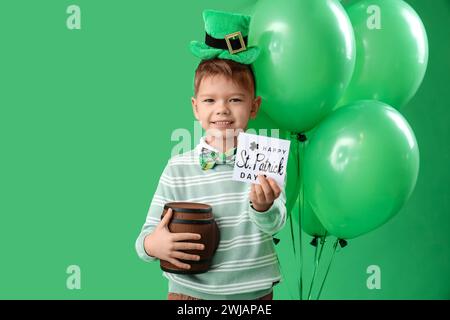 Petit garçon mignon avec chapeau de leprechaun, ballons et carte de voeux pour les équipements Célébration de la fête de Patrick sur fond vert Banque D'Images