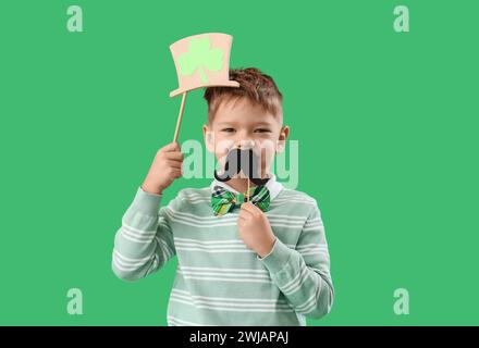 Mignon petit garçon avec chapeau de leprechaun et moustache en papier sur fond vert. Prog Célébration de la fête de Patrick Banque D'Images