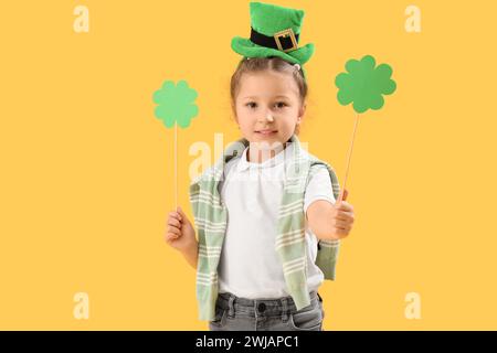 Mignonne petite fille avec chapeau de leprechaun et trèfles en papier sur fond jaune. Prog Célébration de la fête de Patrick Banque D'Images