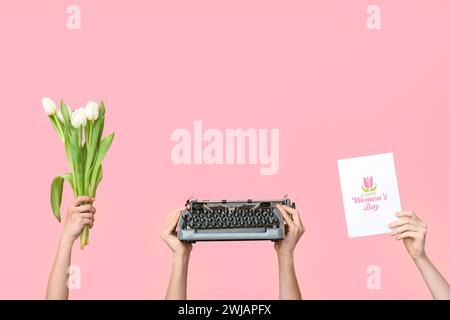Mains tenant machine à écrire vintage, tulipes et carte postale festive avec texte HAPPY WOMEN'S DAY sur fond rose Banque D'Images