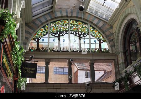 Vitrail semi-circulaire représentant des arbres, des fleurs et des oiseaux au-dessus de l'entrée est de la Royal Arcade, Norwich. Banque D'Images