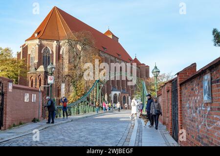 WROCLAW, POLOGNE - 4 NOVEMBRE 2023 : un groupe de touristes non identifiés traverse le pont Tumsky pour rejoindre l'île de sable et une ancienne église gothique. Banque D'Images