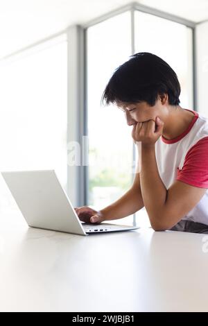 Adolescent asiatique concentré sur son ordinateur portable à la maison, avec espace de copie Banque D'Images