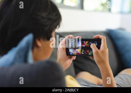 Teenage Asian Boy navigue sur un site de streaming vidéo sur un smartphone à la maison Banque D'Images