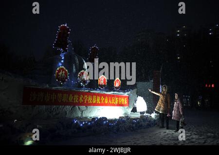 Tacheng, Chine. 14 février 2024. Les visiteurs regardent un spectacle de lanterne de sculpture sur neige réalisé par des élèves d'écoles primaires sur la place culturelle Shawan dans la préfecture de Tacheng, dans la région autonome ouïgur du Xinjiang, au nord-ouest de la Chine, le 12 février 2024. (Photo de Costfoto/NurPhoto) crédit : NurPhoto SRL/Alamy Live News Banque D'Images