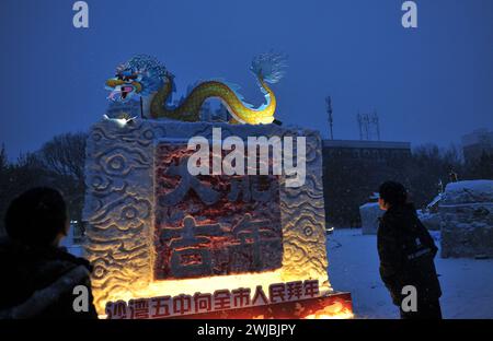 Tacheng, Chine. 14 février 2024. Les visiteurs regardent un spectacle de lanterne de sculpture sur neige réalisé par des élèves d'écoles primaires sur la place culturelle Shawan dans la préfecture de Tacheng, dans la région autonome ouïgur du Xinjiang, au nord-ouest de la Chine, le 12 février 2024. (Photo de Costfoto/NurPhoto) crédit : NurPhoto SRL/Alamy Live News Banque D'Images