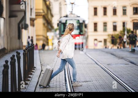 Femme touriste avec valise marche à travers la rue de la ville pendant que le tram arrive. Voyagez prudemment et en toute sécurité avec une assurance et évitez les accidents Banque D'Images