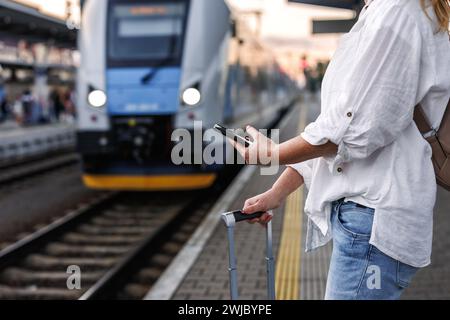 Femme avec valise utilise smartphone et application mobile pour acheter un billet de transport en ligne. Touriste attendant le train à la gare. Voyage solo Banque D'Images