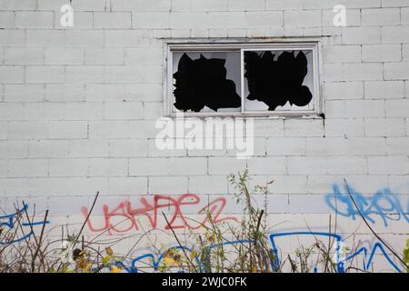 Fenêtres cassées et étiquettes graffiti sur le mur extérieur d'un bâtiment abandonné en blocs de ciment. Banque D'Images