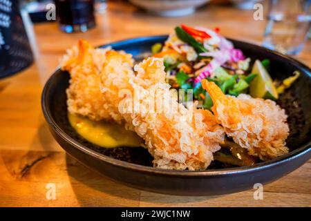 Crevettes tempura frites avec sauce à la mangue et salade dans un bol sur la table avec un verre d'eau. Banque D'Images