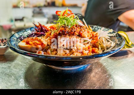 Bol asiatique sucré et aigre avec poulet, crevettes, graines, oeuf et légumes dans un bol bleu sur la table, une partie de l'homme. Banque D'Images