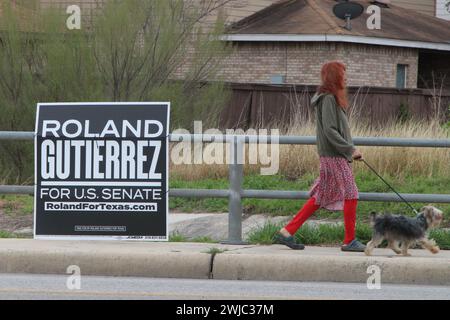 San Antonio, États-Unis. 14 février 2024. Une femme promenant son chien passe devant un panneau de campagne Roland Gutierrez le long de Medina base Road à San Antonio, Texas, États-Unis, le 14 février 2024. Roland Gutierrez est actuellement membre du Sénat du Texas et son district comprend Uvalde, Texas. À la suite de la fusillade de masse de l'école primaire Robb, il a présenté quatre projets de loi sur la sécurité des armes à feu. (Photo de Carlos Kosienski/Sipa USA) crédit : Sipa USA/Alamy Live News Banque D'Images