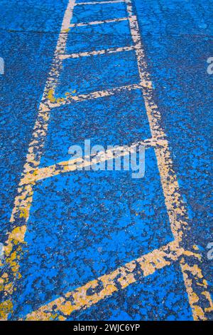 Lignes peintes en jaune sur la surface de la chaussée asphaltée bleue divisant les places de stationnement pour personnes handicapées dans le stationnement. Banque D'Images