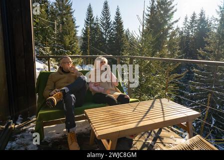 Un homme boit du café et une femme parle au téléphone sur la terrasse de son chalet Banque D'Images