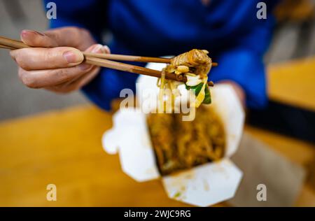 Femme mangeant des nouilles avec des légumes et de la viande de chinois. Banque D'Images