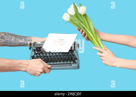 Mains tenant une machine à écrire vintage, des tulipes et une carte postale festive avec texte HAPPY WOMEN'S DAY sur fond bleu Banque D'Images