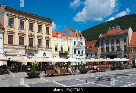 Les gens assis dans des cafés en plein air en face des bâtiments historiques sur une journée ensoleillée dans une ville, maisons de ville à la place du marché Piata Sfatului, vieille ville Banque D'Images