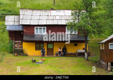 Une maison jaune entourée d'herbe verte avec des gens détendus et des poulets dans la cour avant, les personnes âgées en face d'une maison, Bubesti, Alba Banque D'Images
