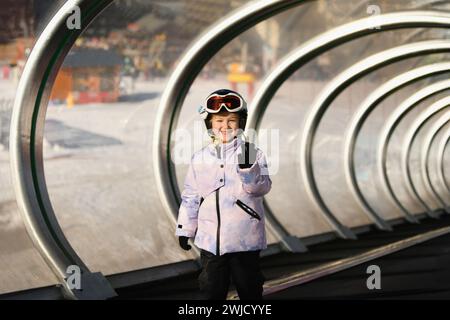 Une fille sur des skis se tient sur un téléski de tapis dans un tunnel de verre Banque D'Images