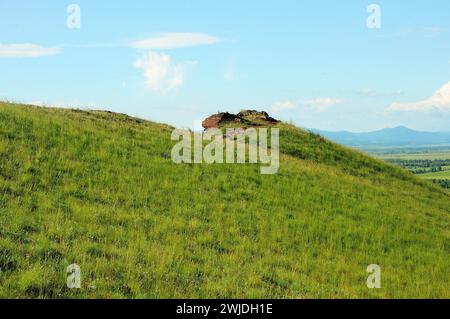 Vestiges d'un ancien mur en ruines de grès stratifié rouge au sommet d'une colline douce surplombant une vallée pittoresque par une journée d'été ensoleillée. Montagne Banque D'Images