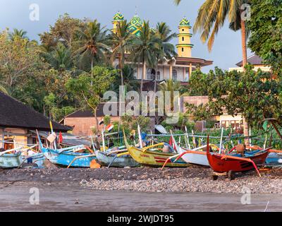 Bateau de pêche traditionnel indonésien avec stabilisateurs au coucher du soleil sur une plage pierreuse à Medewi sur l'île de Bali en Indonésie. Le Jami Masjid Al-Akmal Banque D'Images