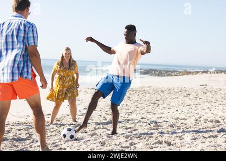 Divers amis apprécient un match de football occasionnel sur la plage Banque D'Images