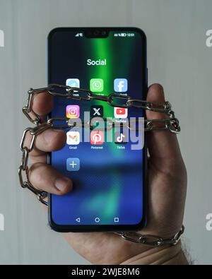 Ouzbékistan, Tachkent - 27 janvier 2024 : chaîne à portée de main avec téléphone mobile avec icônes de réseau social. Concept de limitation du temps sur les réseaux sociaux, addic Banque D'Images