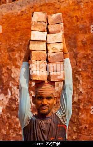 Dhaka, Dhaka, Bangladesh. 15 février 2024. Les ouvriers portent des piles de briques pesant plus de 20 kg sur la tête dans un four à Dhaka, au Bangladesh. Les ouvriers ''“ qui sont payés moins de Â£ 1 par quart ''“ se déplacent jusqu'à 2 500 briques par jour dans des conditions étouffantes. Environ 4 00 000 migrants à faible revenu arrivent à Dacca en provenance de différentes régions du pays chaque année pour travailler à brickfields. Les longues heures de travail sous le soleil brûlant dans les champs de briques, l'accumulation massive de poussière, le risque de tomber des camions et des piles de briques, et le transport de charges excessives posent de graves risques pour la santé du W. Banque D'Images