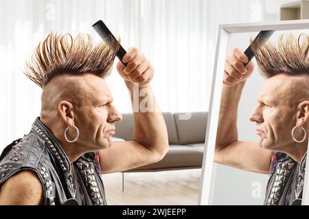 Homme peignant sa coiffure mohawk avec une brosse devant un miroir à la maison Banque D'Images