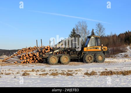 Transporteur forestier Ponsse Wise avec chaînes à neige sur pneus et grumes de pin empilées sur le chantier en hiver. Salo, Finlande. 10 février 2024. Banque D'Images