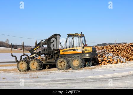 Transporteur forestier Ponsse Wise avec chaînes à neige sur pneus et grumes de pin empilées sur le chantier en hiver. Salo, Finlande. 9 février 2024. Banque D'Images