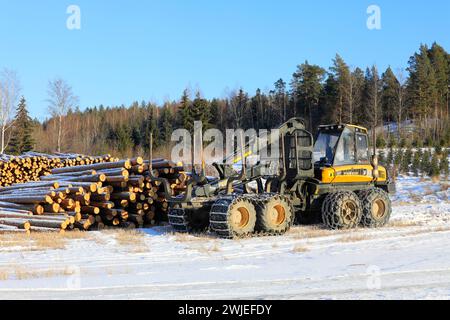 Transporteur forestier Ponsse Wise avec chaînes à neige sur pneus et grumes de pin empilées sur le chantier en hiver. Salo, Finlande. 9 février 2024. Banque D'Images