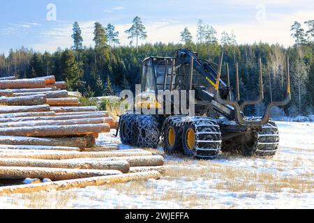 Transporteur forestier Ponsse Wise avec chaînes à neige sur pneus et grumes de pin empilées sur le chantier en hiver. Salo, Finlande. 9 février 2024. Banque D'Images