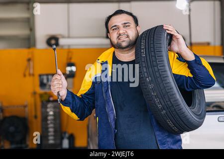 Portrait travailleur indien d'homme dans le garage mécanicien automatique heureux service de voiture de travail remplacer l'entretien de véhicule de pneu Banque D'Images