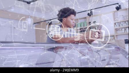 Image d'icônes de médias sur l'assistant de magasin biracial masculin à l'aide d'un smartphone Banque D'Images