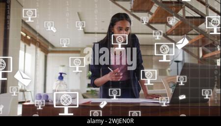 Image d'icônes et de traitement de données sur la femme d'affaires biraciale travaillant dans le bureau Banque D'Images