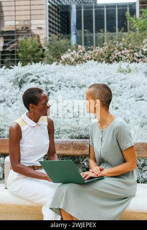 deux femmes d'affaires travaillant avec un ordinateur portable et parlant dans le parc Banque D'Images