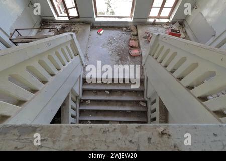 355 escalier intérieur d'une ancienne école primaire abandonnée pleine de gravats, verre manquant de fenêtre, livre rouge sur le sol. Vevchani-Macédoine du Nord. Banque D'Images