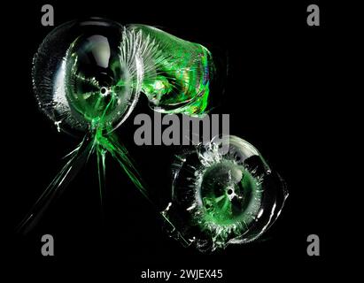 Verre fissuré. Trous de balle avec des reflets verts dans le verre sur fond noir. Macro. Vue latérale. Banque D'Images