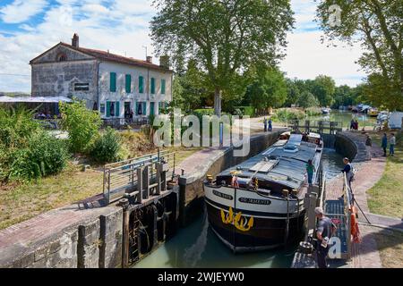 Gardouch (sud-ouest de la France) : péniche de fret passant par l'écluse de Gardouch et la maison du gardien transformée en restaurant le long du canal Banque D'Images