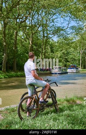 Couple sur une balade à vélo le long du canal, péniche et maison de gardien d'écluse convertie en restaurant "la bonne Planque". Le canal du midi est enregistré Banque D'Images