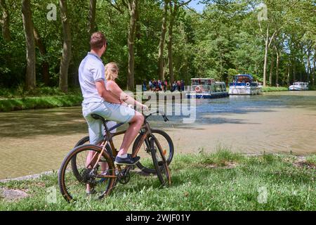 Couple sur une balade à vélo le long du canal, péniche et maison de gardien d'écluse convertie en restaurant "la bonne Planque". Le canal du midi est enregistré Banque D'Images