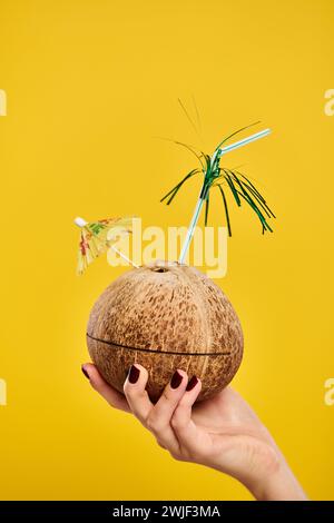 objet photo de cocktail dans la noix de coco fraîche décoré avec parapluie dans la main de la femme inconnue Banque D'Images