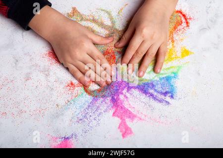Mains d'enfant jouant avec du sable coloré arc-en-ciel. Motricité, concept de créativité infantile. Banque D'Images
